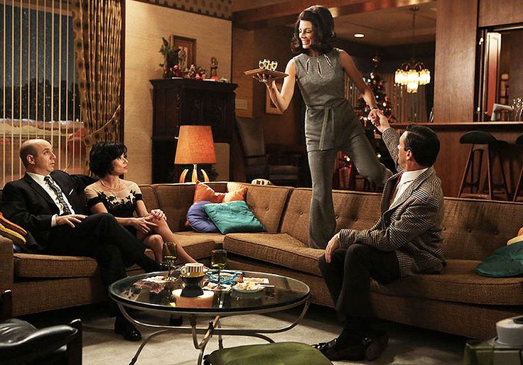 a woman standing on top of a couch in a living room next to two men