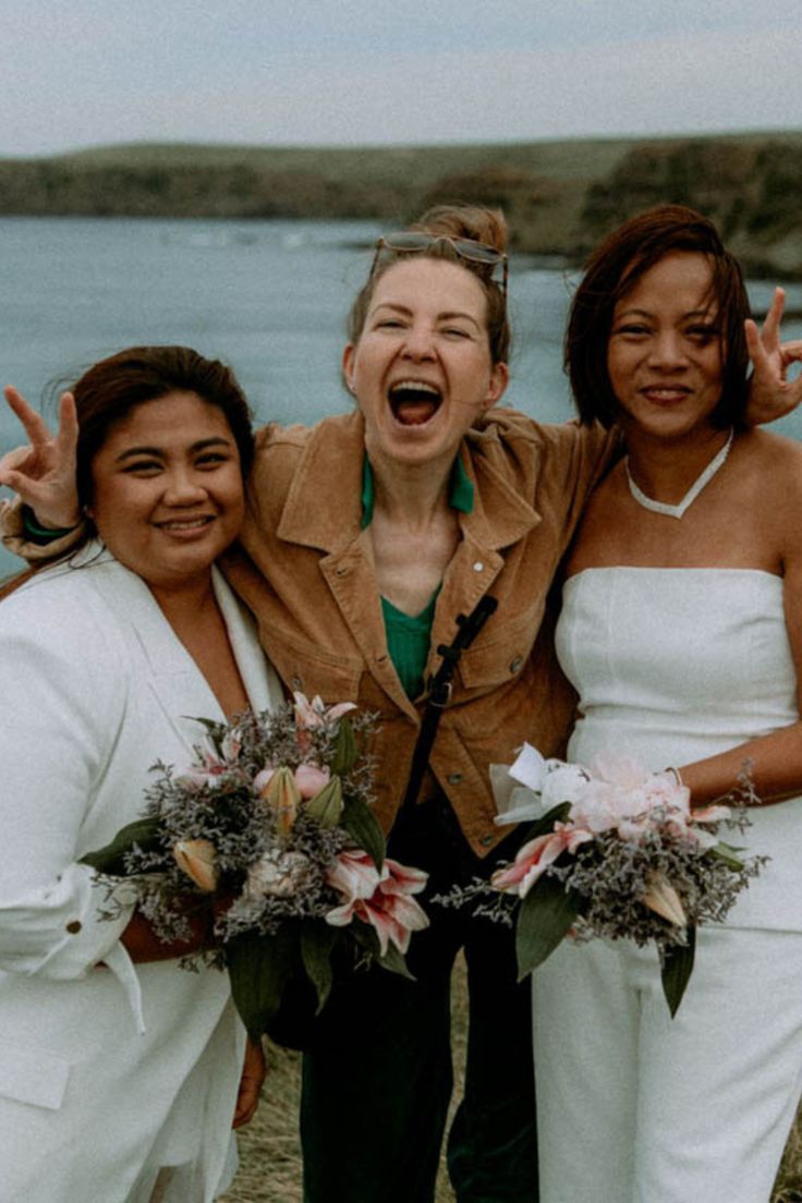 three women standing next to each other with their arms in the air and one woman holding flowers