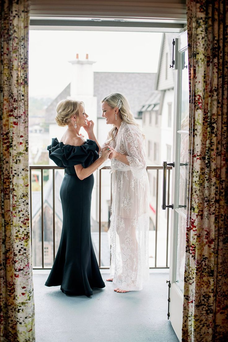 two women standing in front of a window looking at each other while one woman holds her hand up to her mouth