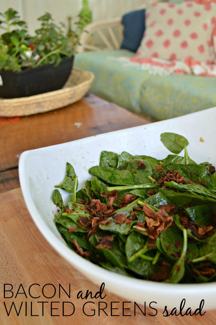 a bowl filled with spinach and bacon on top of a wooden table next to a couch