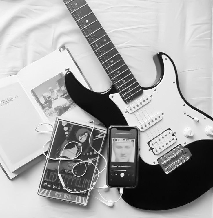 an electric guitar, book and mp3 player on a bed