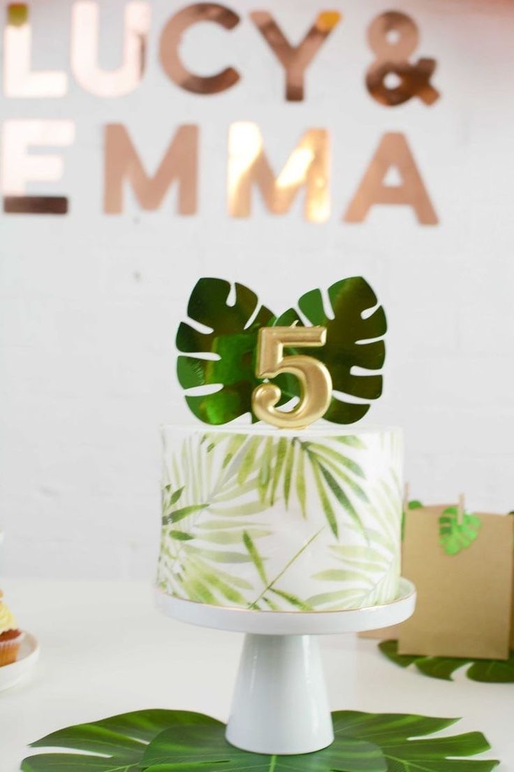 a white cake topped with a green leaf covered number five on top of a table