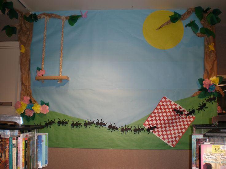 a bulletin board is decorated with flowers and bugs on the grass in front of a blue sky