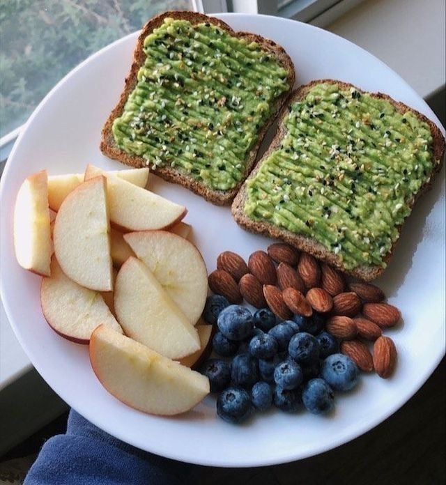 a white plate topped with two pieces of bread and fruit next to almonds, blueberries, and an avocado