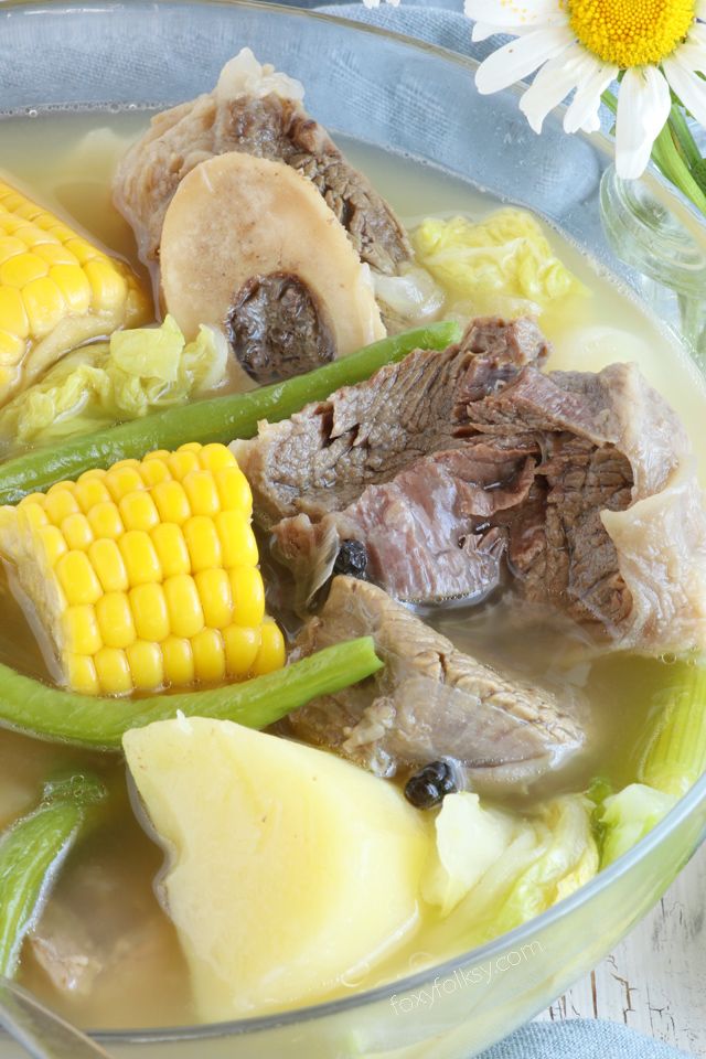 a bowl filled with meat and vegetables on top of a table next to a daisy