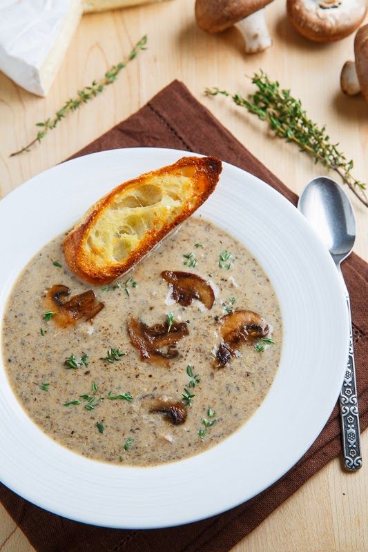 a white plate topped with mushroom soup next to a piece of bread on top of a wooden table