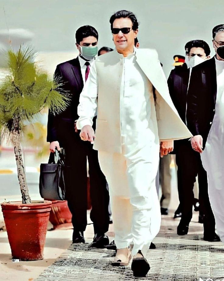 a man wearing a face mask walks down the street with other men in suits and ties