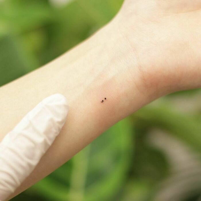 a small black dot tattoo on the wrist