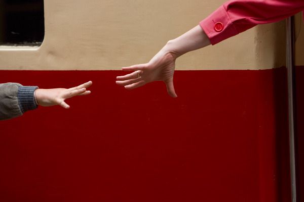 two people reaching out their hands to touch each other's hand on a red and beige wall