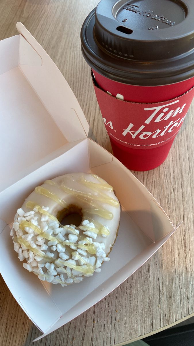 a donut in a box next to a cup of coffee