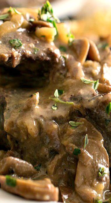 a white plate topped with meat and mushrooms covered in gravy, garnished with parsley