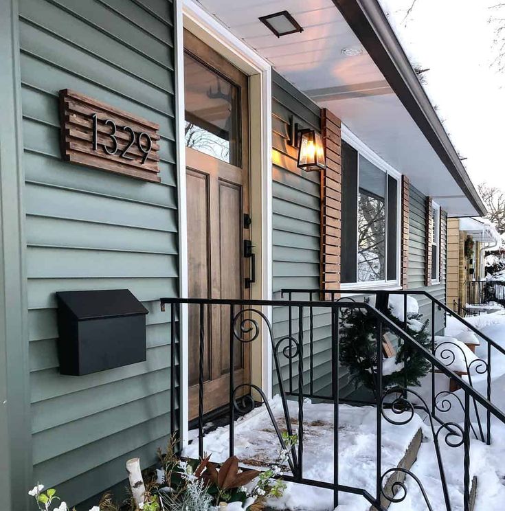 a house with snow on the ground next to it's front door and mailbox