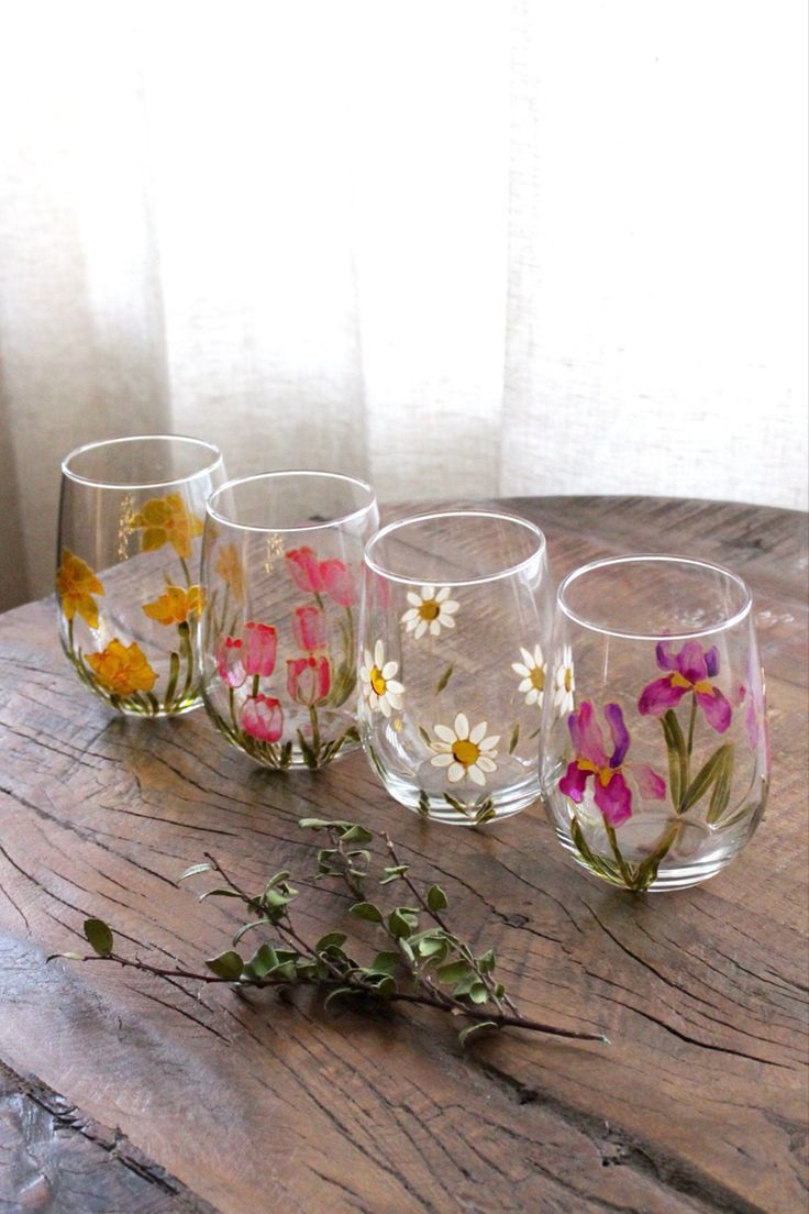 four glasses with flowers painted on them sitting on a table