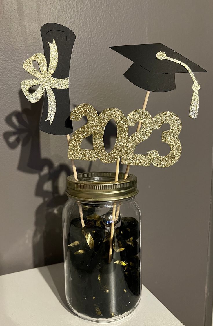 a mason jar filled with black and gold graduation decorations