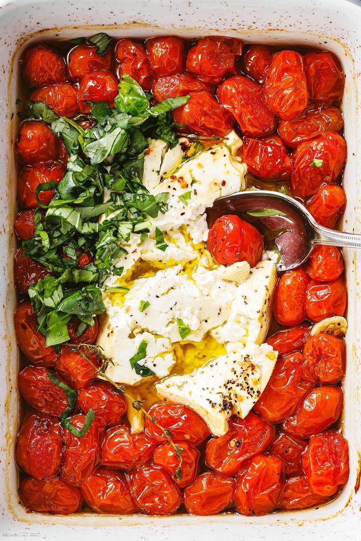 tomatoes and other vegetables in a casserole dish with a serving spoon on the side