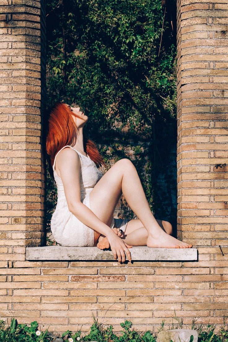 a woman with red hair sitting on a window sill