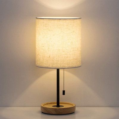 a table lamp with a wooden base and a white linen shade on the top of it