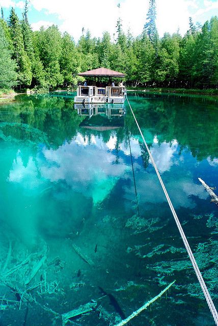 a boat floating on top of a lake surrounded by trees and blue water with clouds in the sky