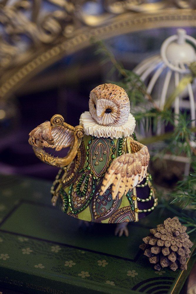 an owl figurine sitting on top of a green table next to pine cones