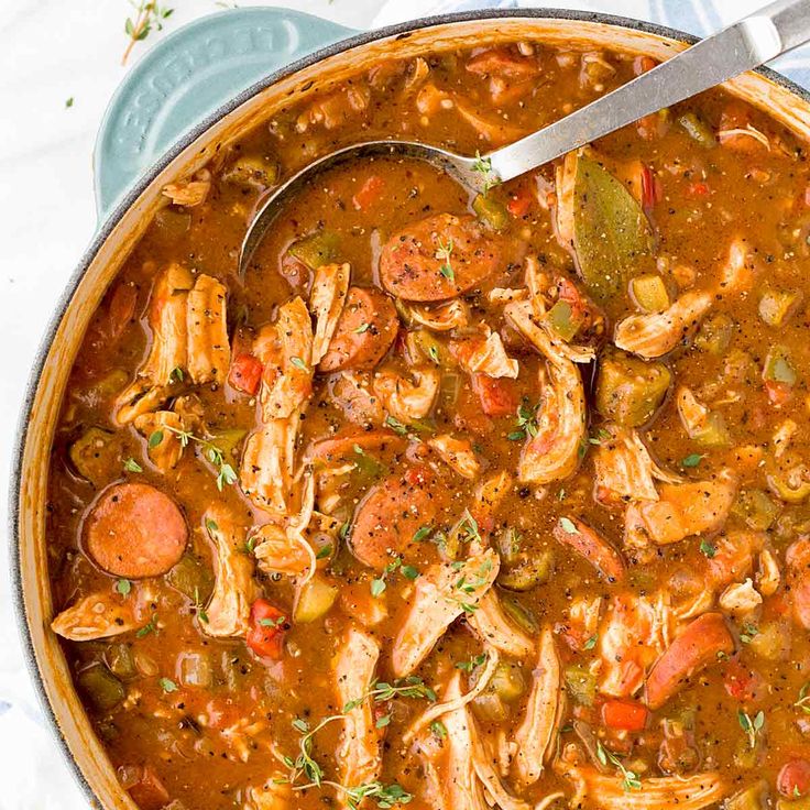 a pot filled with chicken and vegetable soup on top of a white table cloth next to a spoon