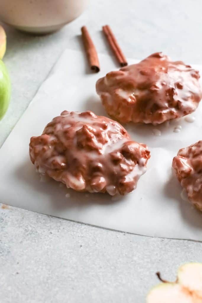 three donuts with chocolate glaze and cinnamon sticks on a paper towel next to an apple