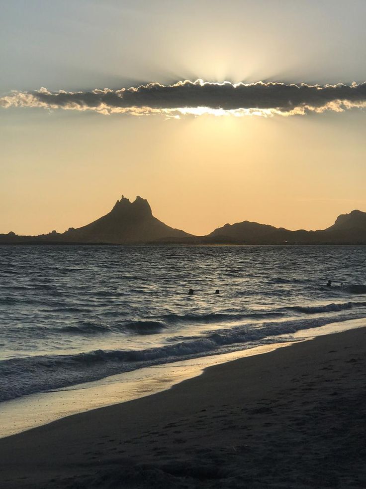 the sun is setting over an ocean with mountains in the distance and people swimming in the water