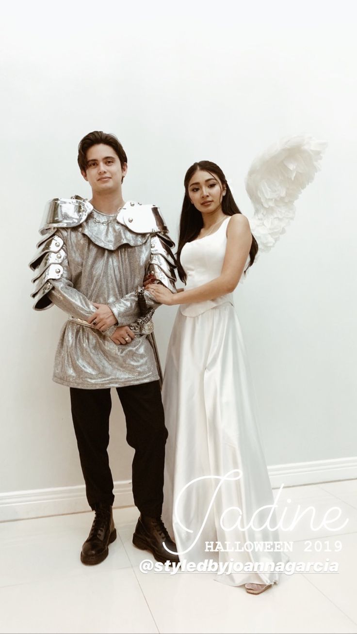 a man and woman dressed up as knight and angel standing in front of a white wall