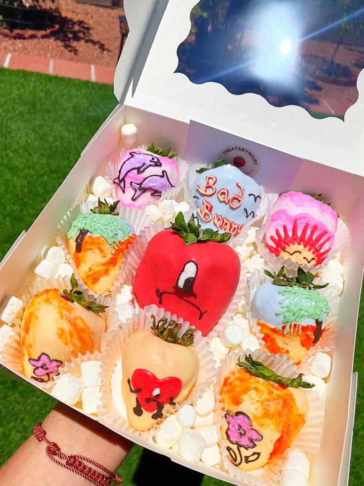 a box filled with lots of cupcakes on top of a lush green field