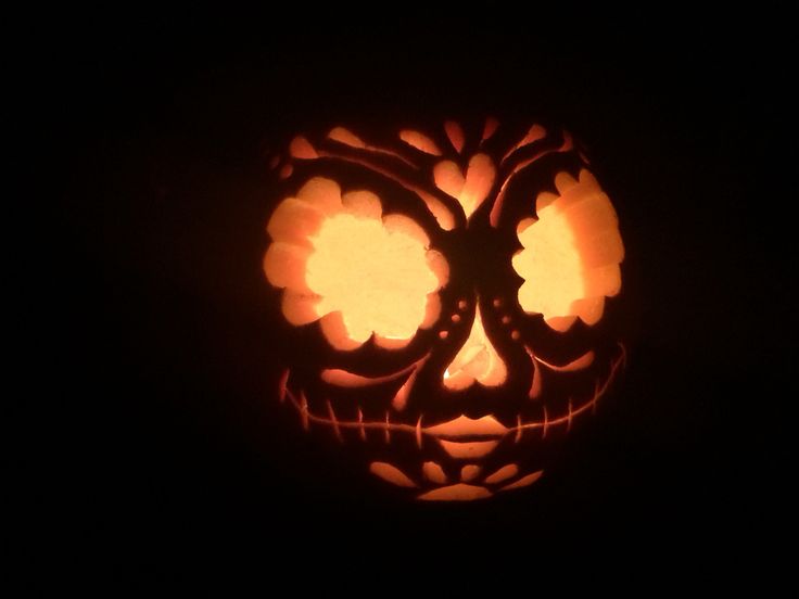 a pumpkin carved to look like a skull with glowing eyes and flowers in its mouth