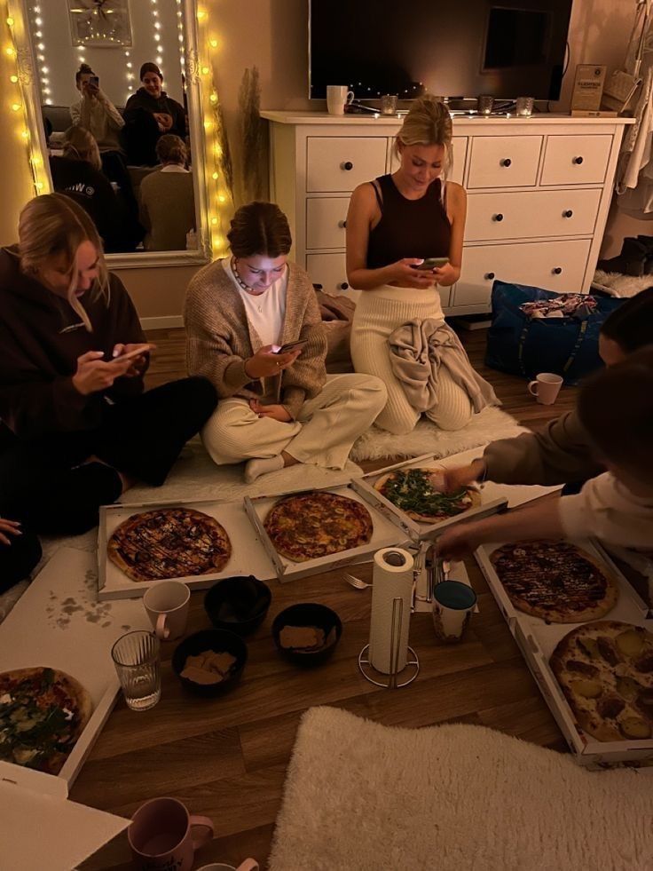 several people sitting on the floor with food in front of them and one person looking at her phone