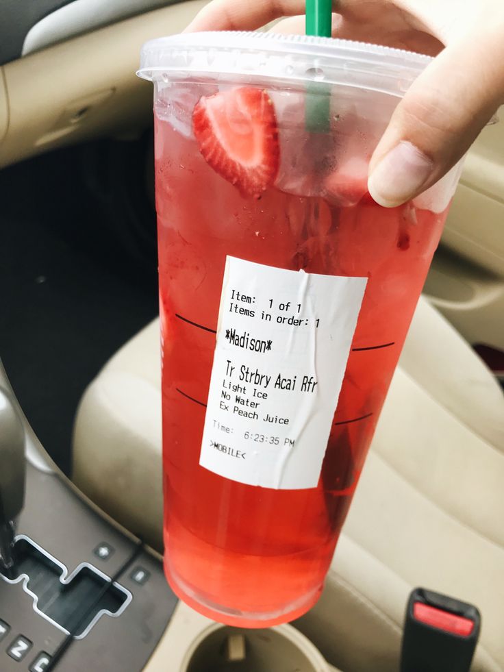 a person holding up a drink with strawberries on the rim in a car seat