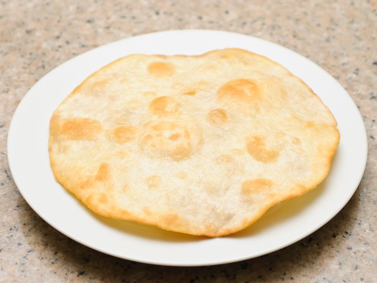 a white plate topped with a flat bread on top of a marble countertop next to a knife and fork