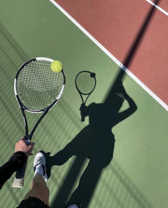 the shadow of a person holding a tennis racket and ball on a tennis court