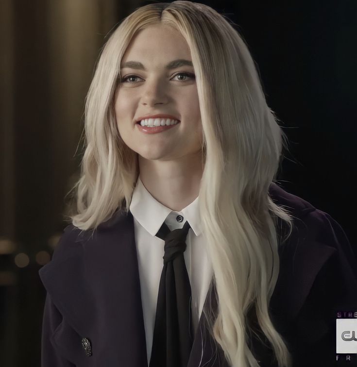 a woman with long blonde hair wearing a black tie and white shirt smiling at the camera