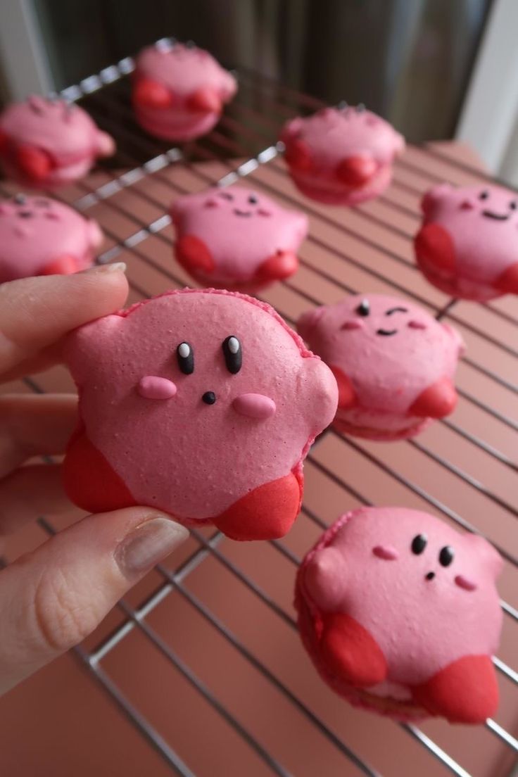 a person holding up some pink cookies with faces on them in front of a rack