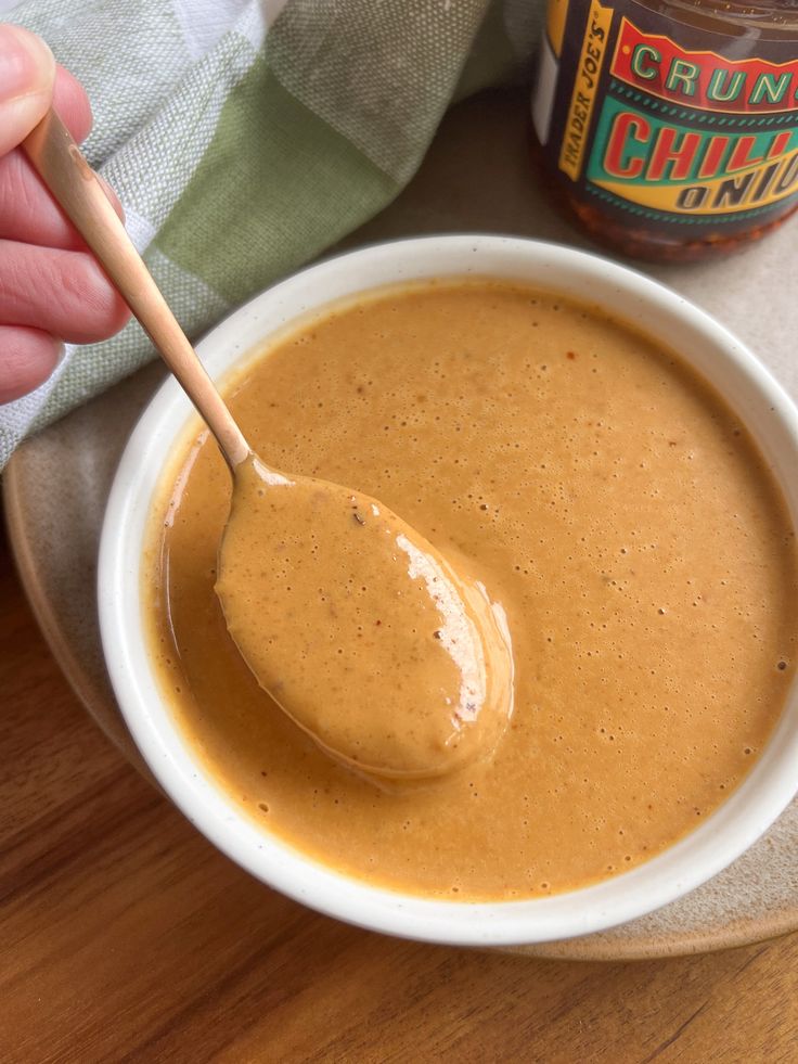 a person holding a spoon over a bowl of peanut butter on top of a wooden table