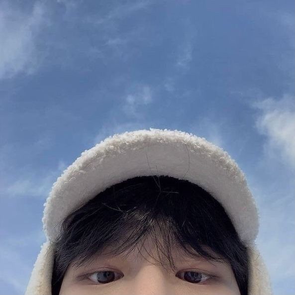 a young boy wearing a white hat and jacket looking up at the camera with a blue sky in the background