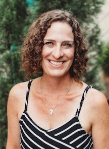 a woman with curly hair wearing a black and white striped dress smiling at the camera