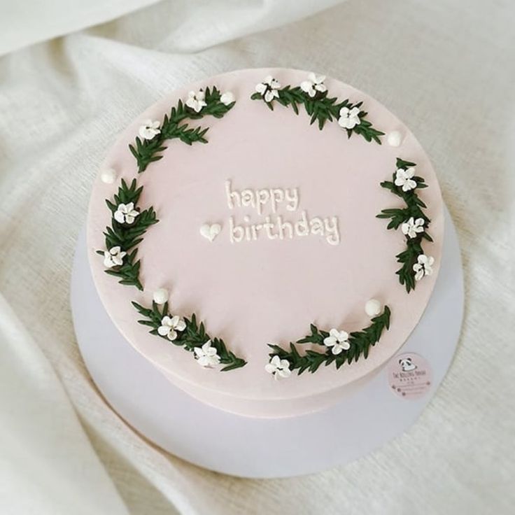 a pink birthday cake with white flowers and greenery on it's side that says happy birthday