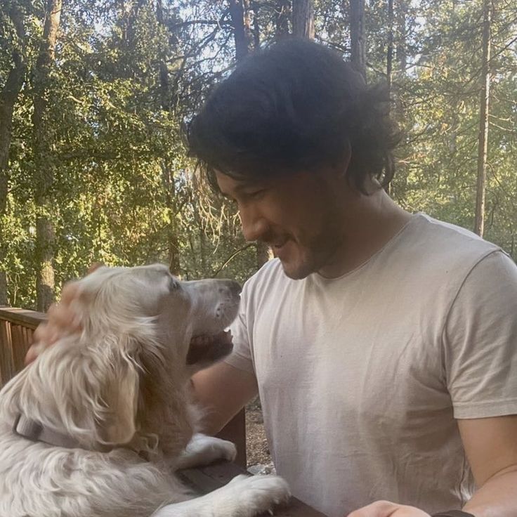 a man petting a white and brown dog in the woods on a sunny day