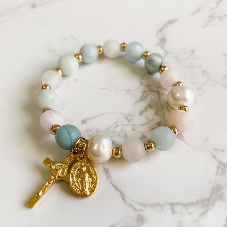 This decade rosary stretch bracelet is made with 8mm matte aquamarine and rose quartz gemstone beads, stretch cord, 10mm pearls, gold plated spacer beads and gold tone Italian made crucifix and Miraculous medal charms. The bracelet is 7 inches in length. Please send me an Etsy message if you need a different size. The bracelet will come packaged in a jewelry box to keep it safe on its journey to you. It's also perfect for gifting and would be a great addition to an Easter basket! Follow us on In Beads Packaging Ideas, Catholic Bracelet, Sacred Jewelry, Rosary Jewelry, Decade Rosary, Bracelets Design, First Communion Gifts, Catholic Rosary, Catholic Jewelry