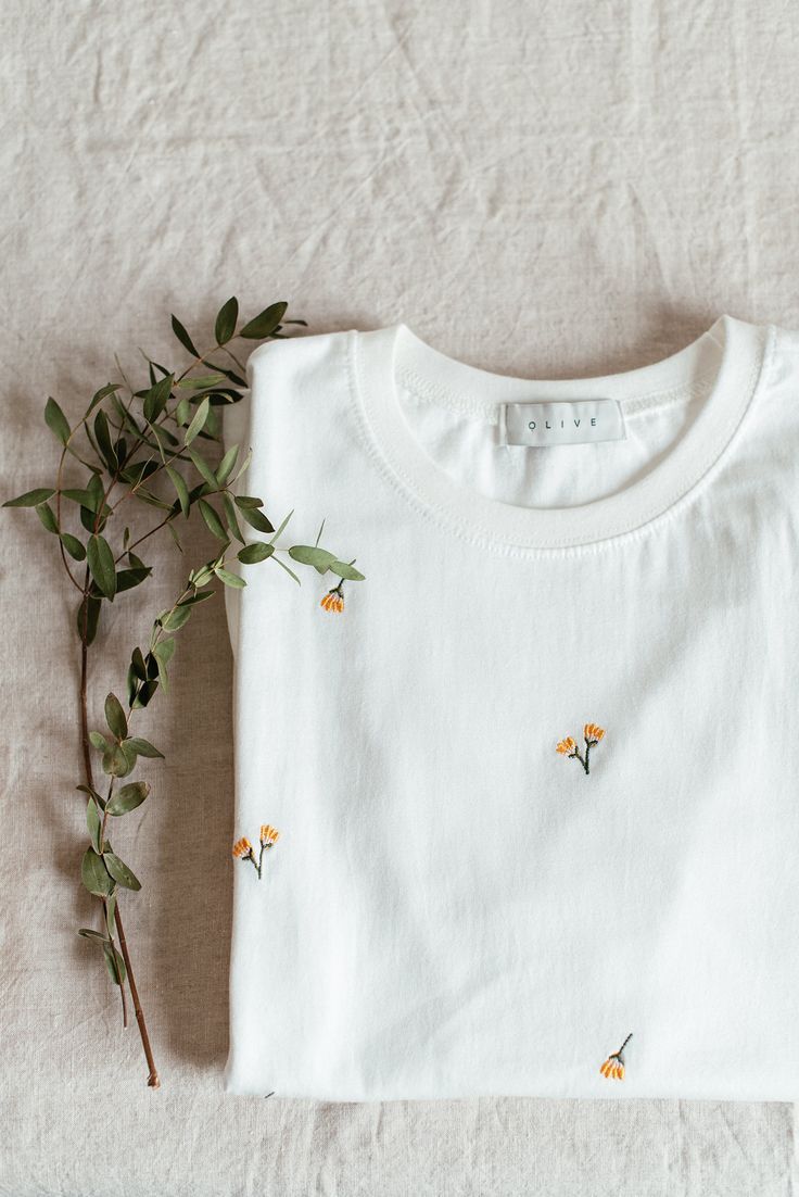 a white t - shirt with small yellow flowers on the front and back, sitting next to a plant