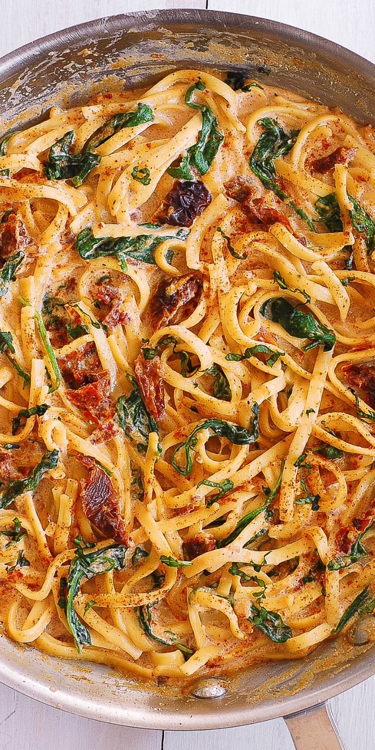 a pan filled with pasta and spinach on top of a wooden table