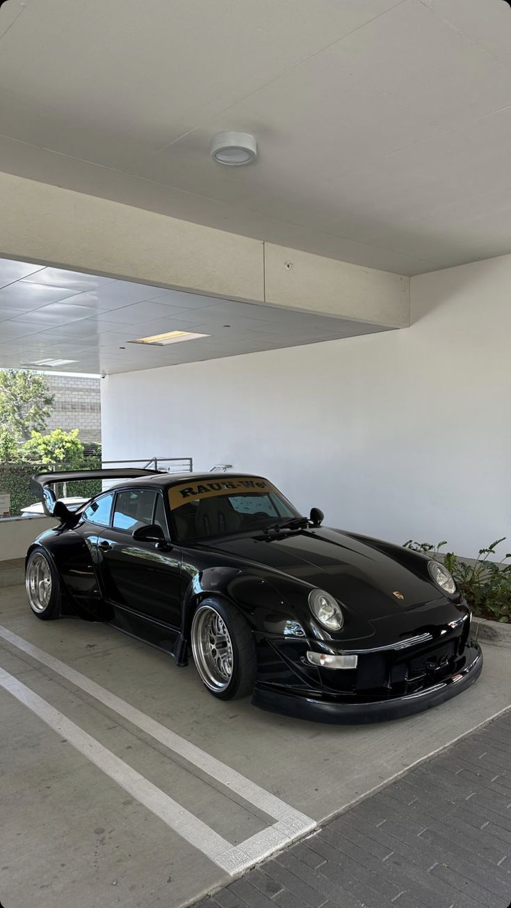 a black sports car parked in a parking lot next to a white wall and potted plants