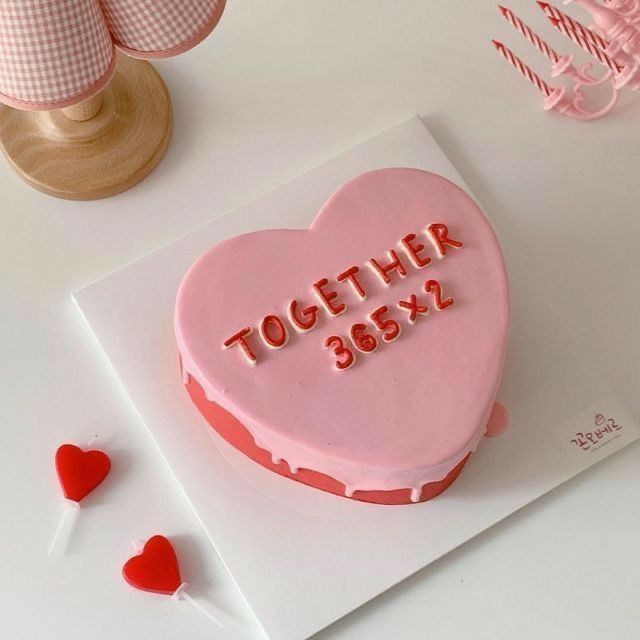 a pink heart shaped cake with the words together 3655x on it and two red hearts next to it