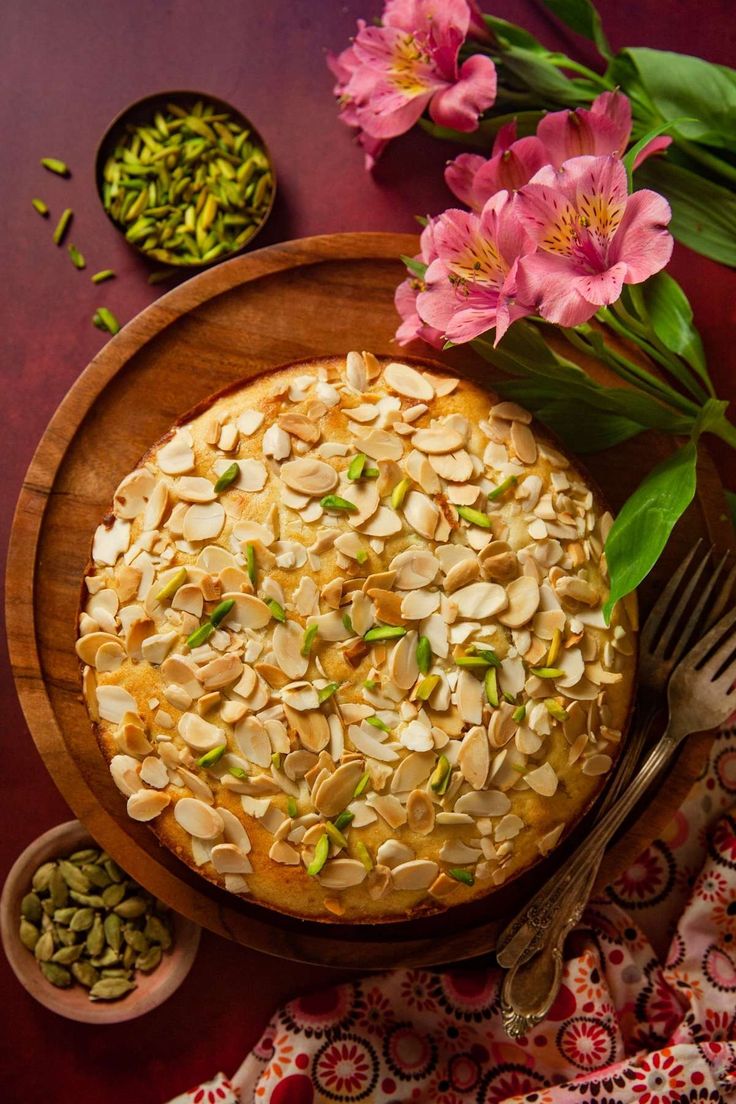 a cake with almonds and pistachio nuts on a wooden plate next to flowers