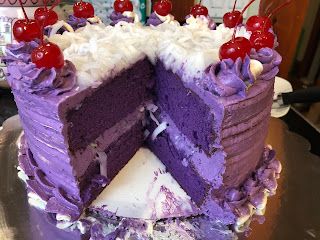 a purple cake with white frosting and cherries on the top is cut in half