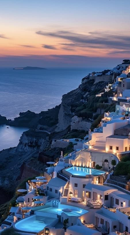 an aerial view of the ocean and buildings at dusk, with lights on all sides