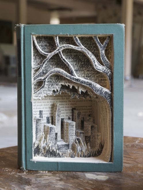 an altered book with trees and buildings in the pages is on top of a table