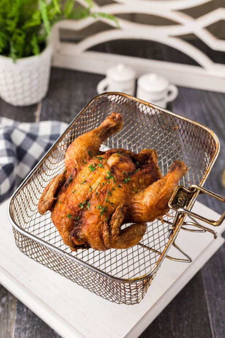 a roasted chicken in a wire basket on a wooden table